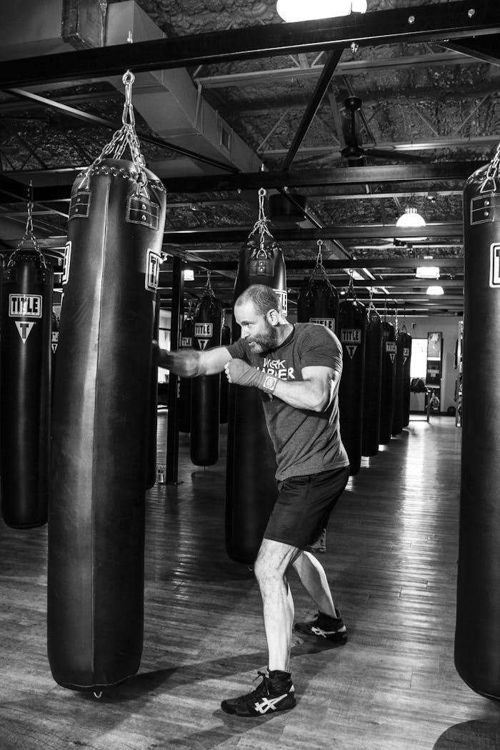 menu-02 A man boxing with a punching bag in a gym, captured in black and white.